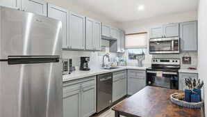 A modern kitchen with stainless steel appliances, grey cabinets, and a wooden dining table.