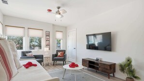 A living room with a sofa, a coffee table, a TV, a ceiling fan, and a plant.