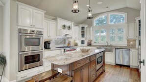 A kitchen with white cabinetry, stainless steel appliances, a marble countertop, and a large window. - 5 32nd Avenue by Avantstay Gourmet Kitchen Pool Balconies (Isle of Palms)