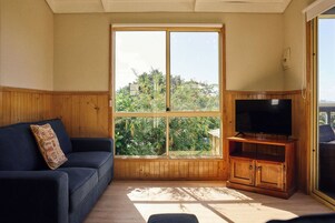 A room with a large window, a wooden cabinet with a television, and a dark blue sofa.