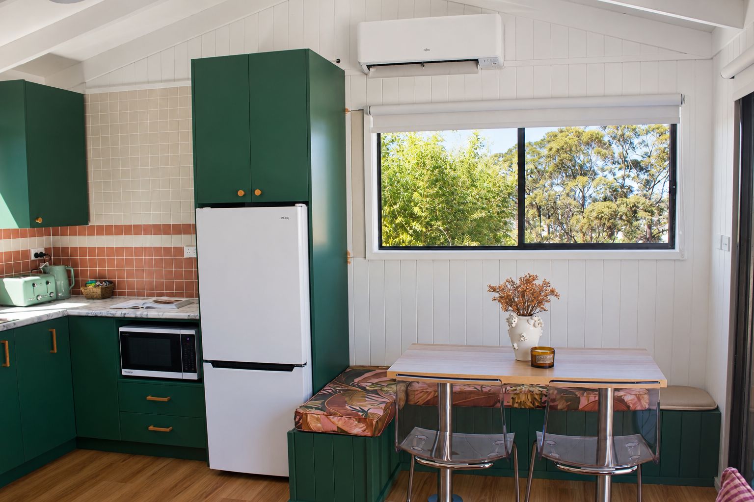 Una cocina con gabinetes verdes, un refrigerador blanco, una estufa y un ventanal con vistas a árboles.