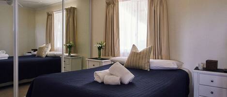 A hotel room with a large bed, a bedside table, a mirror, and a window with curtains.
