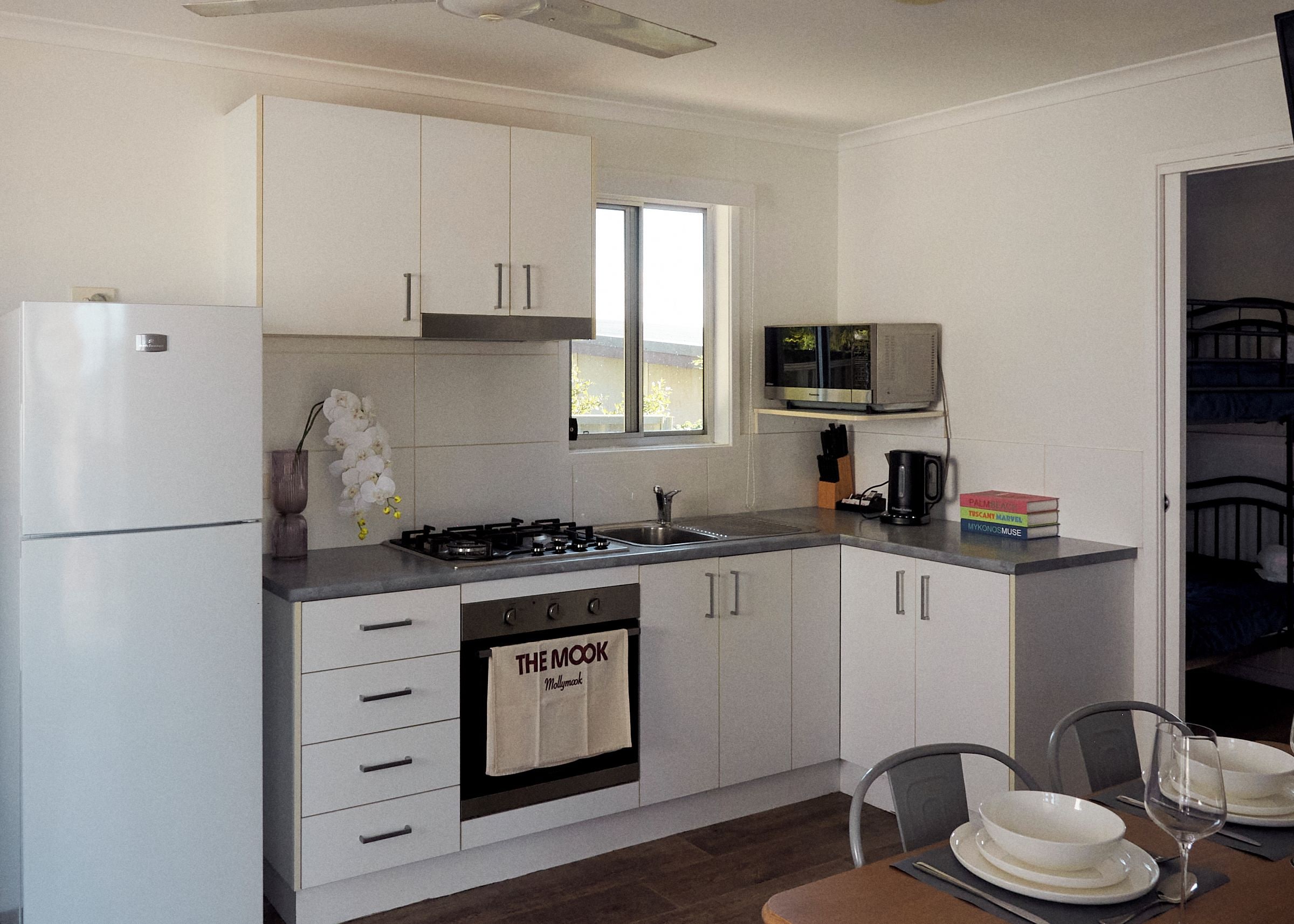 Una cocina compacta equipada con refrigerador, estufa y microondas, y un pequeño comedor con una mesa para dos.