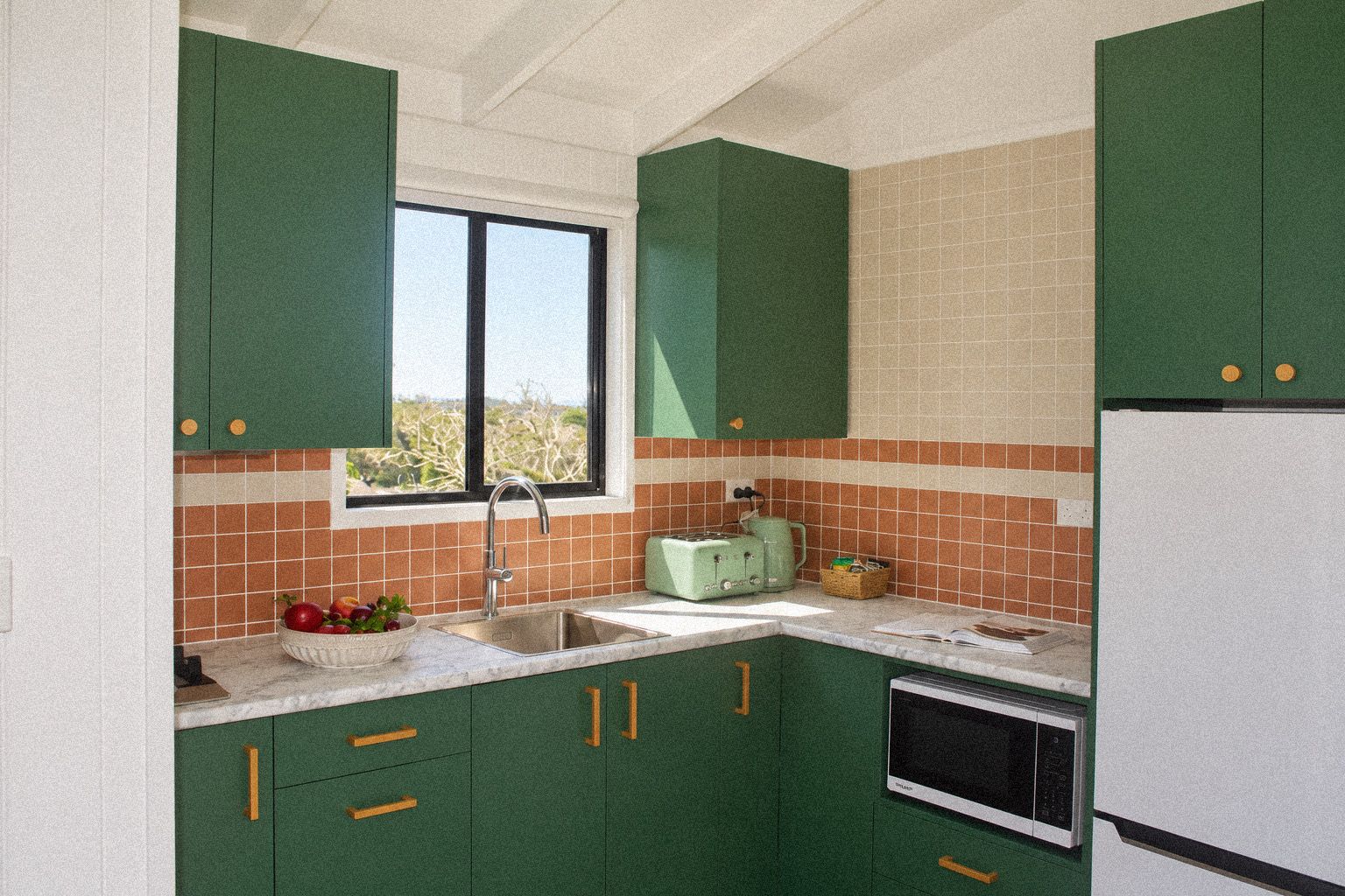 Eine Küche mit grünen Schränken, einem Fenster, einer Spüle, einem Toaster und einem Kühlschrank.