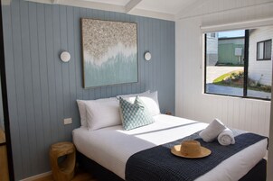 Un dormitorio con cama, almohadas, una manta, un sombrero y una ventana con vistas al exterior.