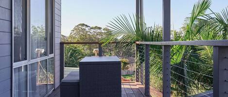 A covered outdoor area with a wooden deck, a wicker table, and a view of greenery and trees.
