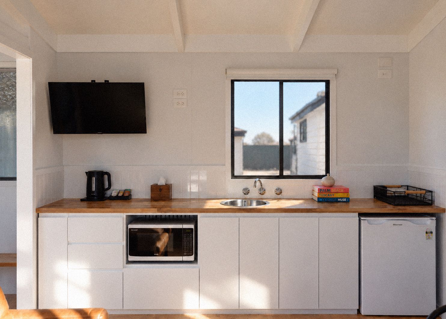 Cocina compacta con horno integrado, lavamanos y ventana con vistas a una casa.