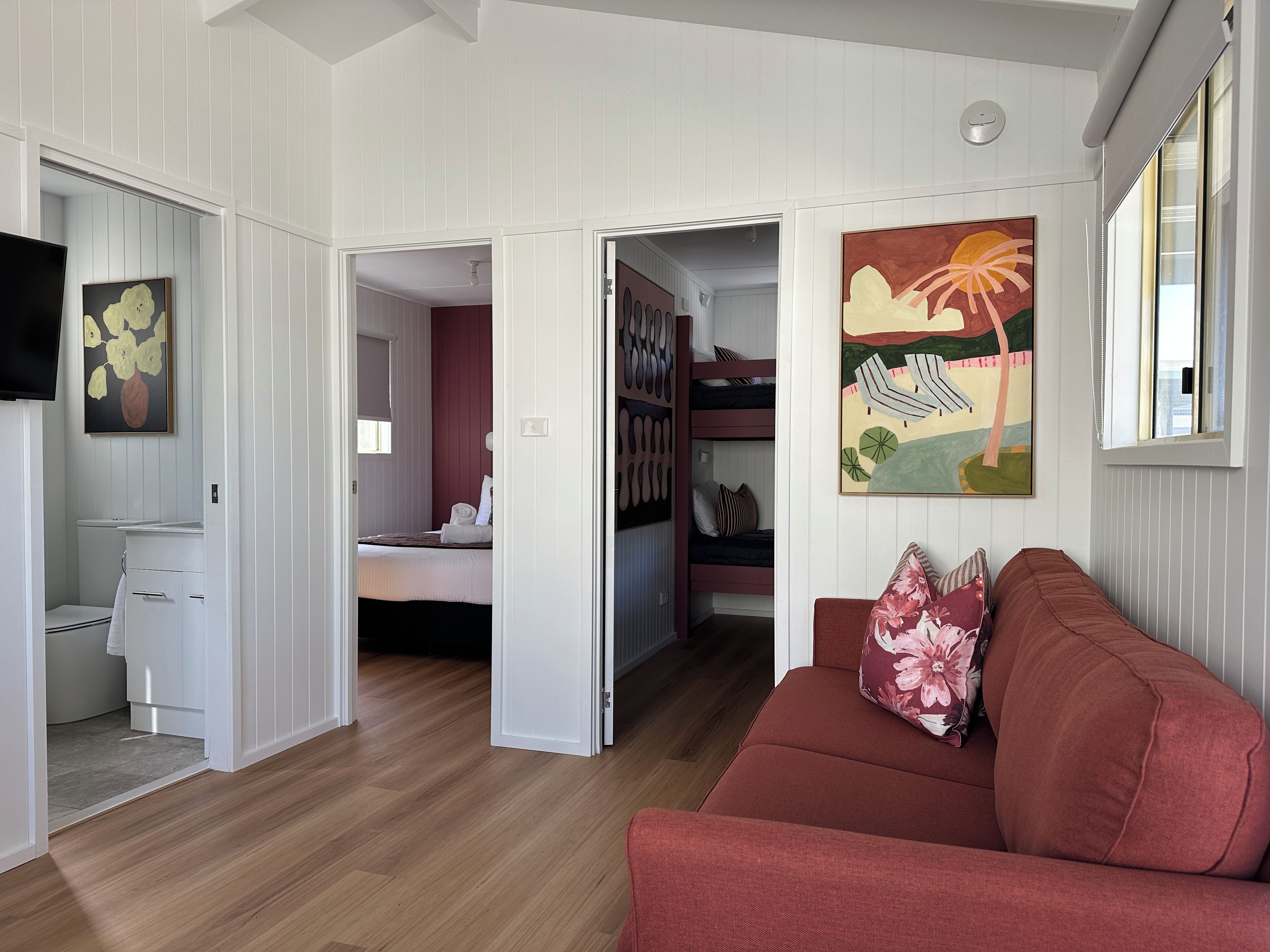 A room with a red sofa, a painting, and a bunk bed with pillows.