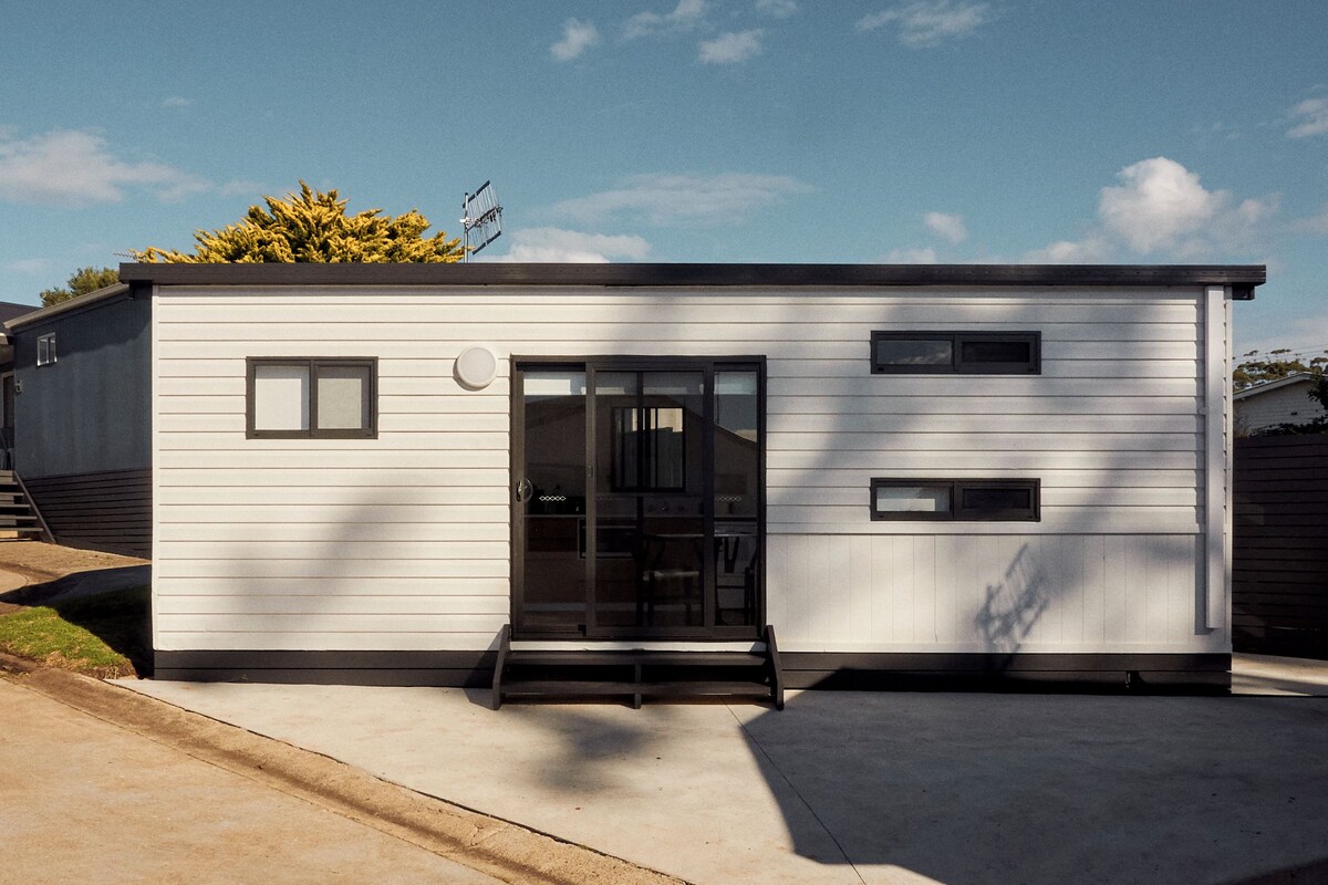 A modern single-story building with a black door, two windows, and a small porch.