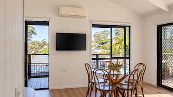 Una habitación con una mesa de comedor, sillas, un televisor y ventanas amplias con vistas a una zona residencial.