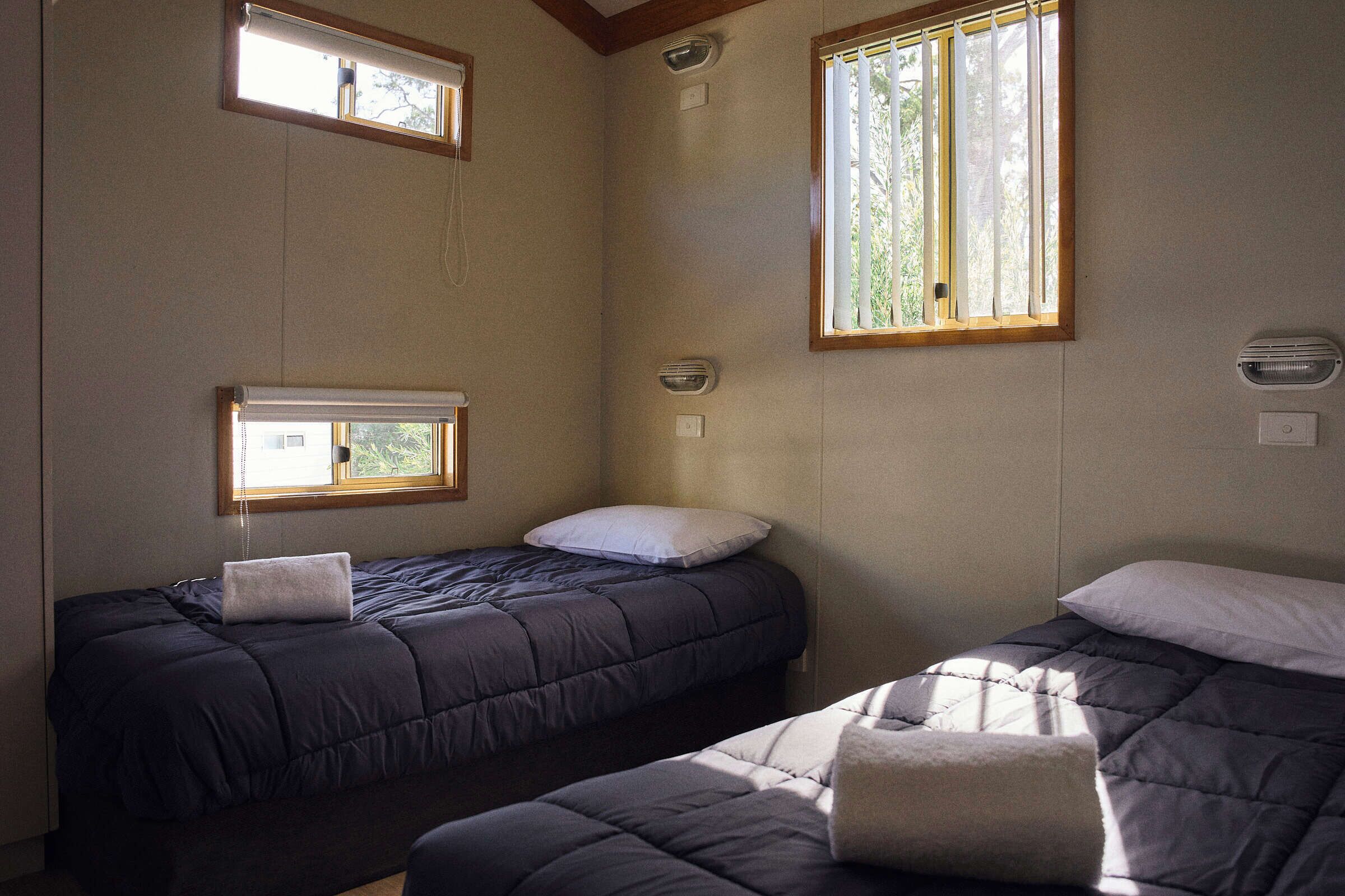 Una habitación con dos camas, una ventana y una lámpara fijada a la pared.