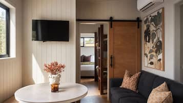 A room with a white round table, a dark sofa, a mounted TV, and a sliding door leading to another room.