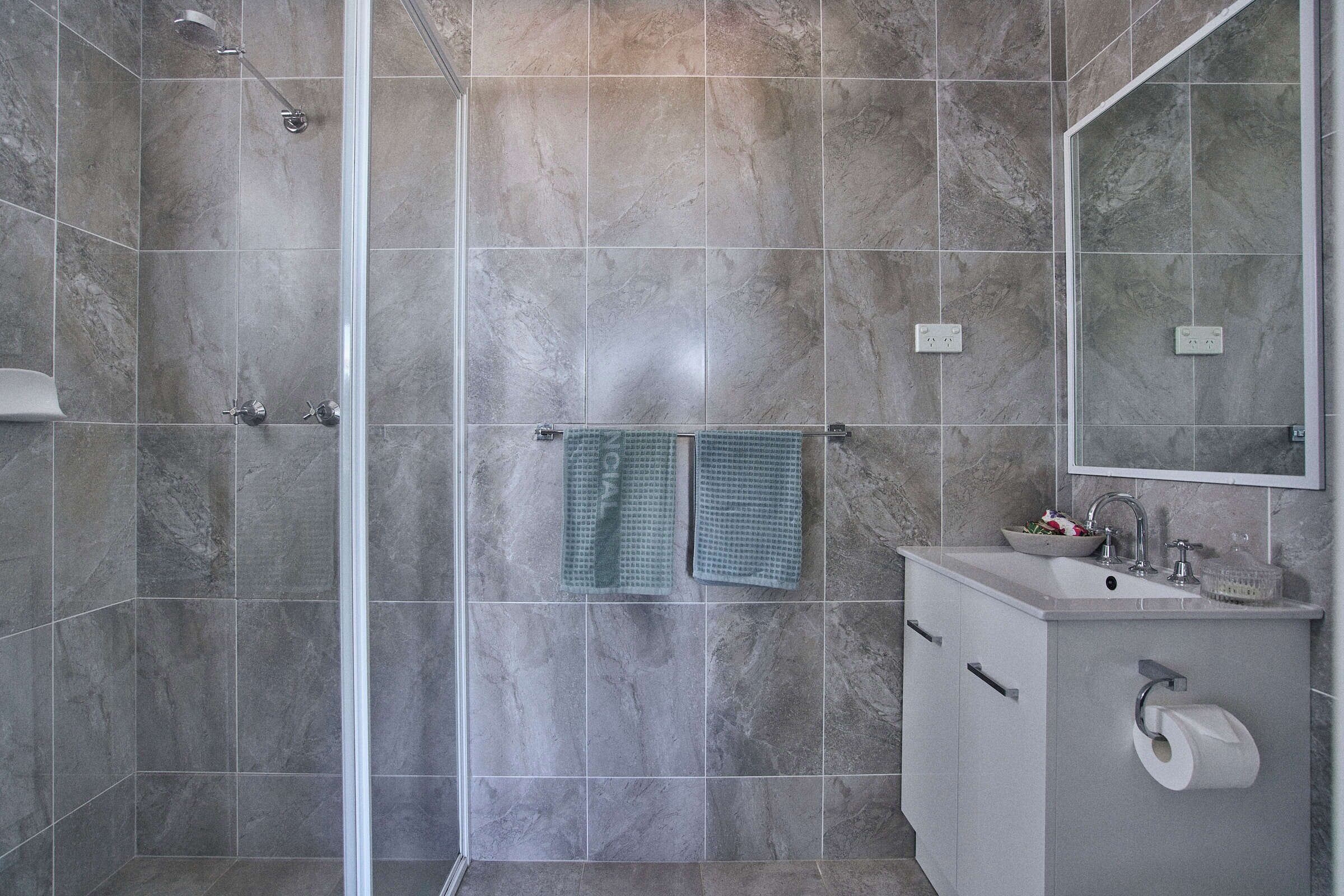 Un bagno con doccia, lavandino, specchio e porta asciugamani.
