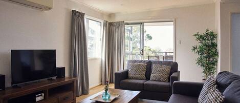 A living room with a flat-screen TV, wooden coffee table, sofa, and a potted plant.