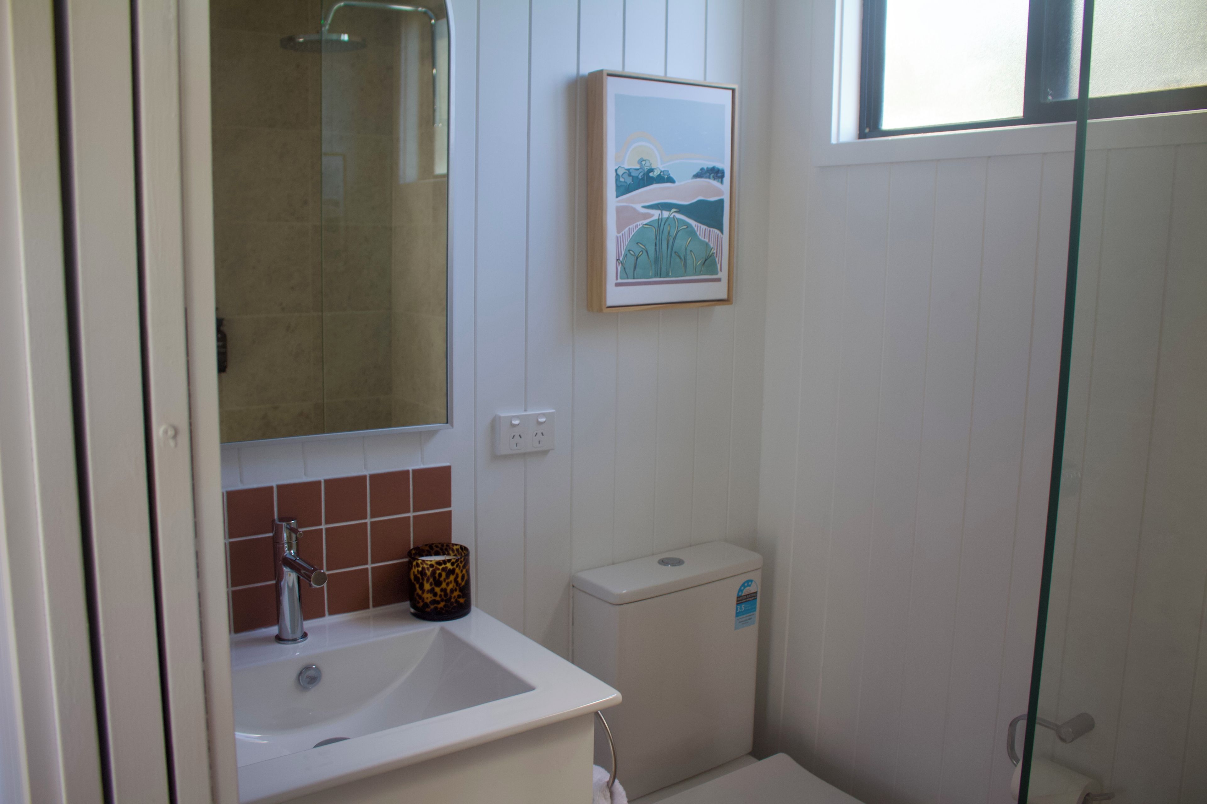 Un baño con lavamanos, espejo, inodoro y un cuadro en la pared.