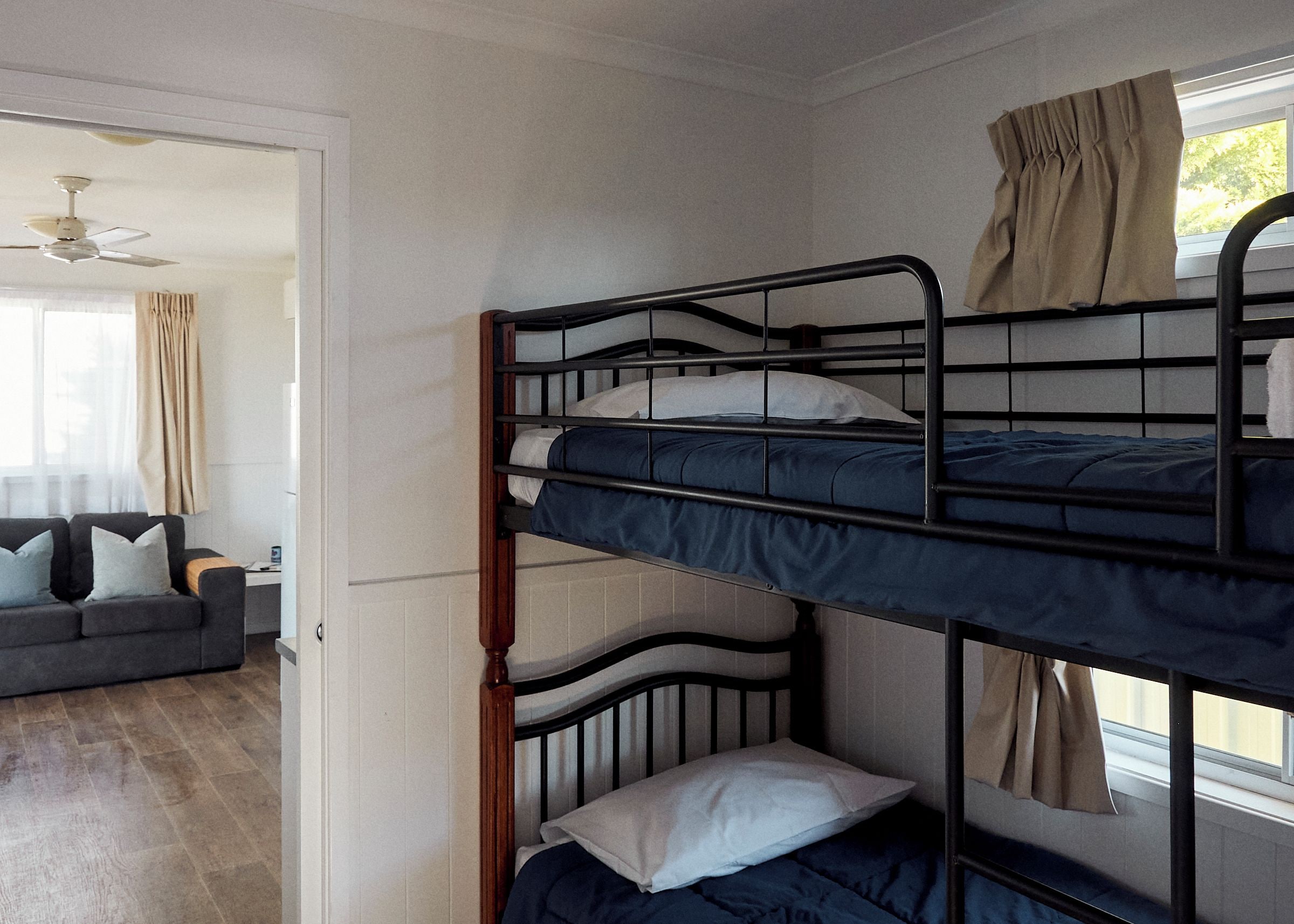 A bunk bed room with a window, a ceiling fan, and a sofa in the adjacent room.