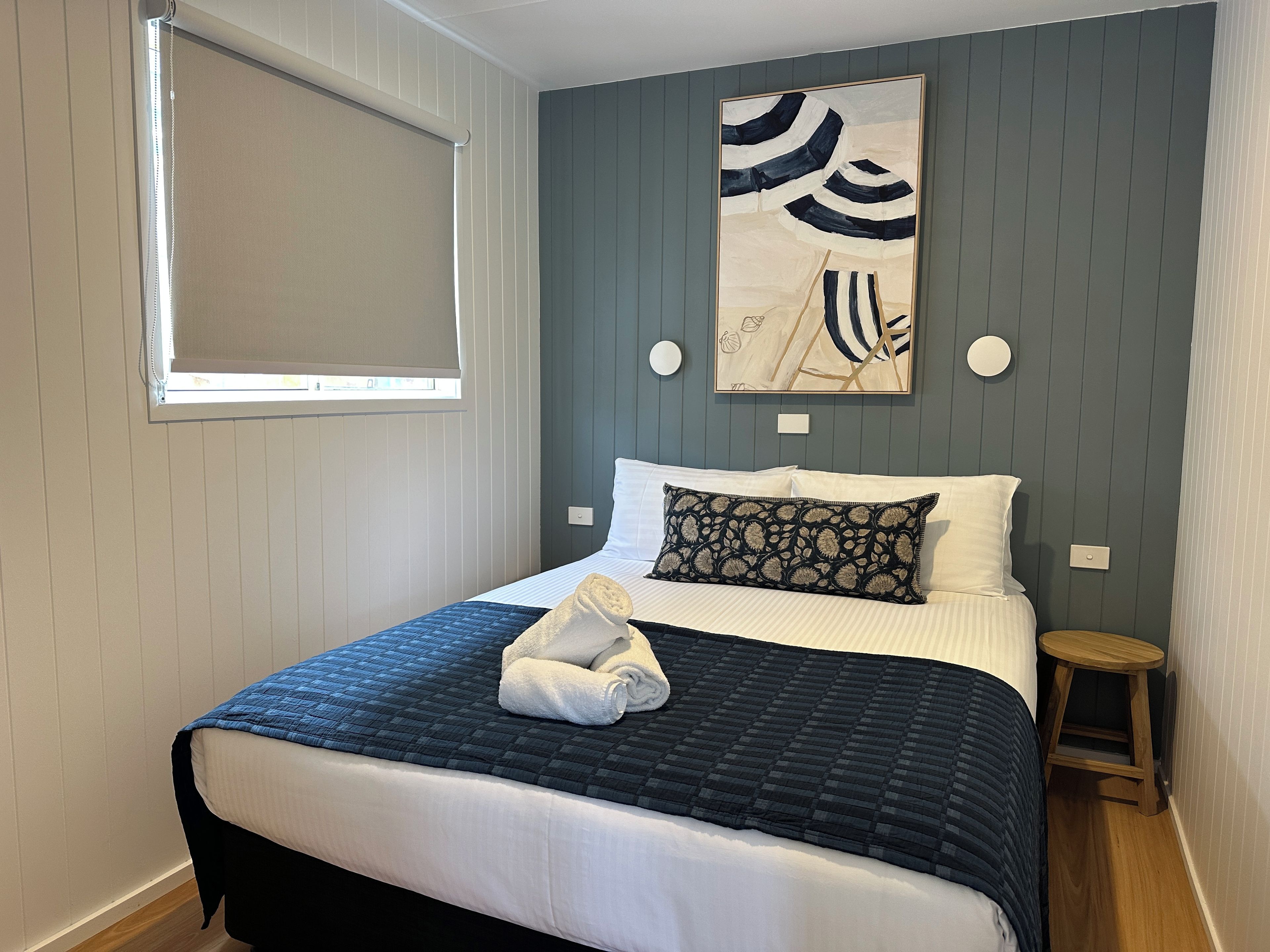 A neatly made bed with a blue quilt, white pillows, and a decorative pillow with a leaf pattern.