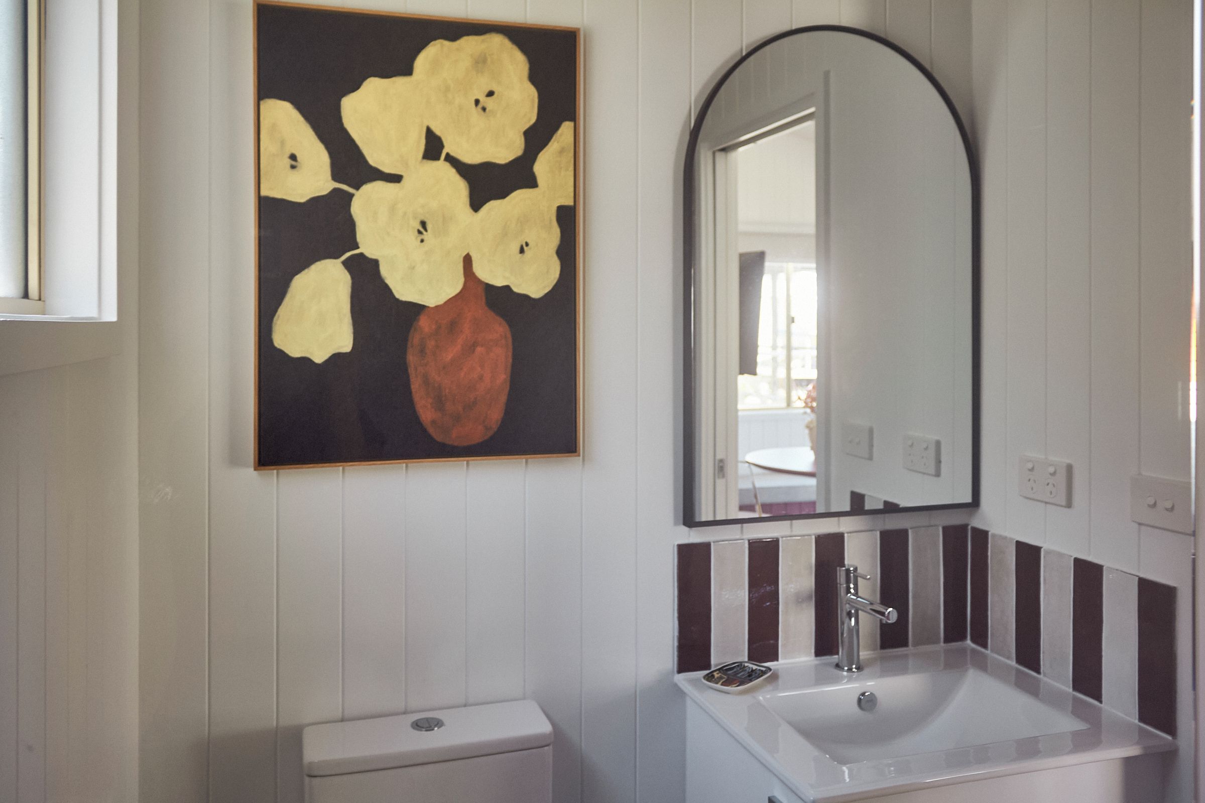 A bathroom with a white sink, a mirror, and a painting of flowers on the wall.