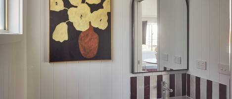 A bathroom with a white sink, a mirror, and a painting of flowers on the wall.