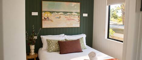 A bedroom with a bed, pillows, a vase with flowers, and a painting on the wall.