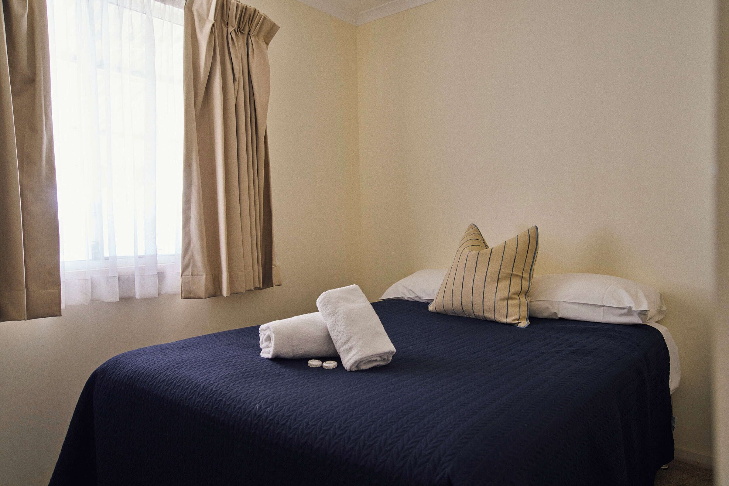 A hotel room with a bed, pillows, and a window with curtains.