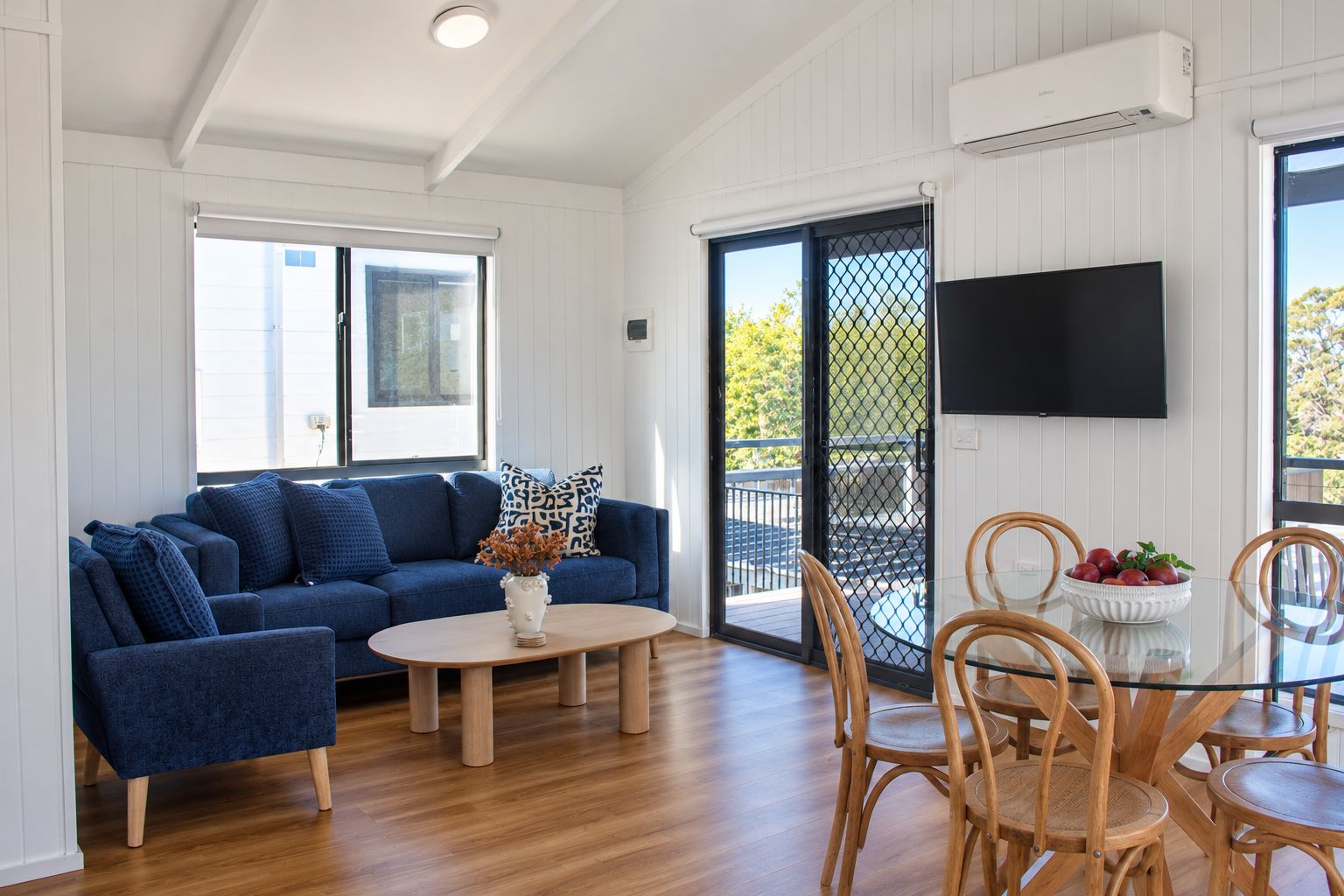 A living room with a blue sofa, a coffee table, and a dining area with chairs and a glass table.