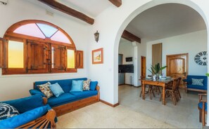 A cozy living room with a blue sofa, wooden dining table, and an arched doorway leading to another room.