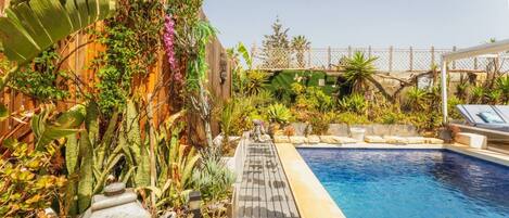 A pool area with a wooden deck, various plants, and a fence in the background.