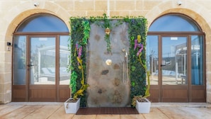 A stone facade with two arched doorways, a central stone wall with a water feature, and potted plants. - Tal Jordan Complex - Bungalow 3 Frog (Gharb)