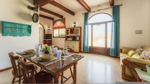 A dining area with a wooden table and chairs, a kitchen in the background, and a sofa in the living area. - Tal Jordan Complex - Bungalow 3 Frog (Gharb)