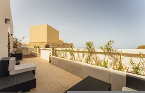 Eine Dachterrasse mit Sitzgelegenheiten im Freien, einem Grill und Blick auf das Meer.