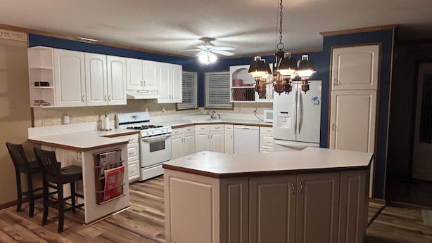 A kitchen with white cabinets, a stove, a refrigerator, and a ceiling fan.