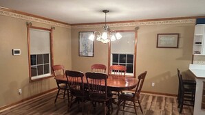 A dining room with a wooden table and chairs, a chandelier, and a window with a view.