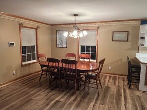 A dining room with a wooden table and chairs, a chandelier, and a window with a view.