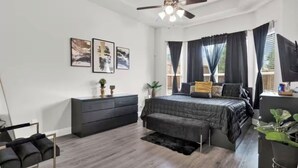 Ein Schlafzimmer mit Bett, Kommode, Deckenventilator und gerahmten Bildern an der Wand.