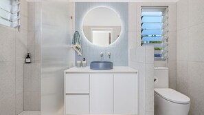 Et moderne badeværelse med et rundt spejl, en vask og et toilet.