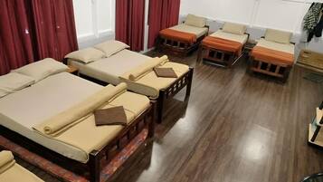 A room with multiple beds arranged in a row, wooden flooring, and a window with curtains.