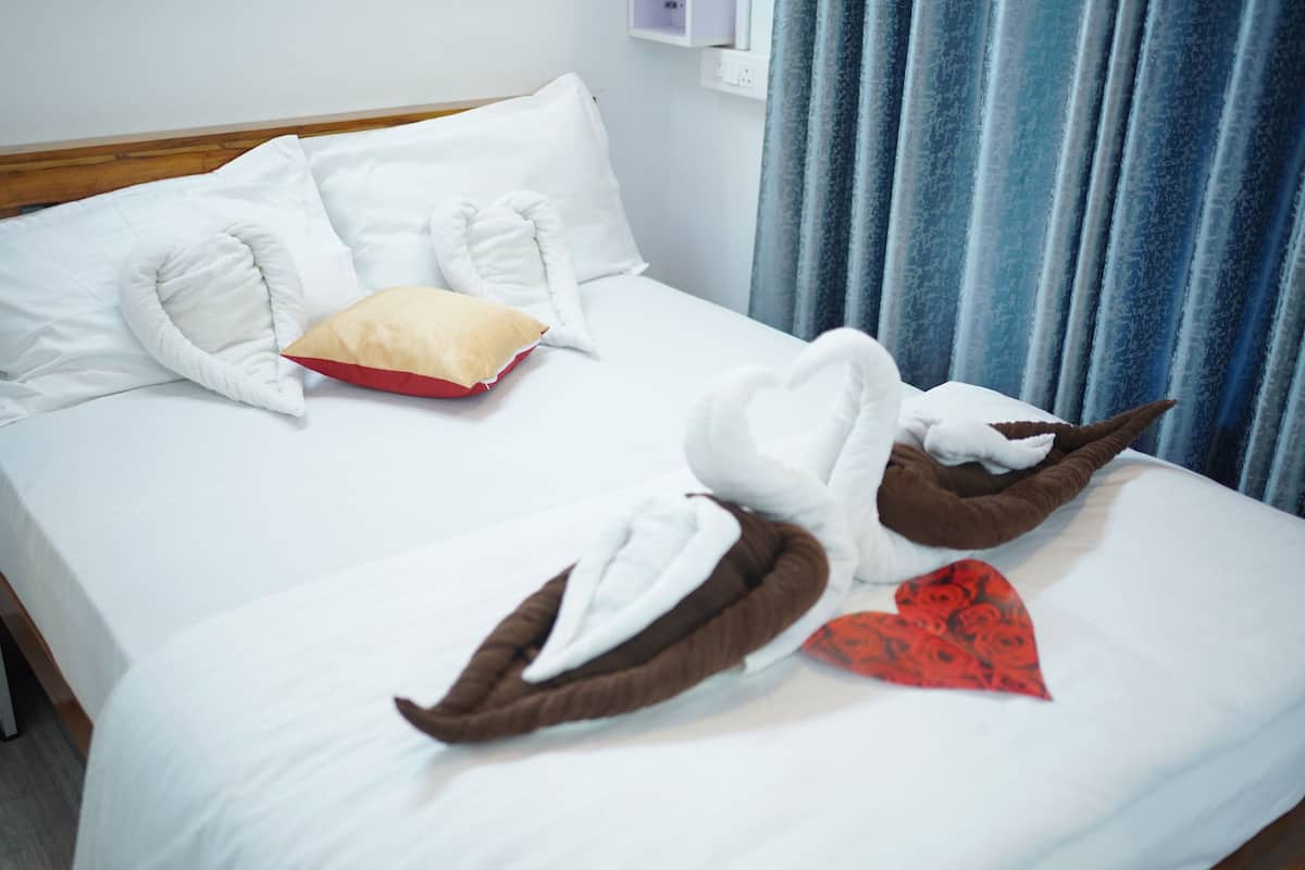 A neatly made bed with white and brown towels arranged in a heart shape, a red heart-shaped pillow, and a white pillow.