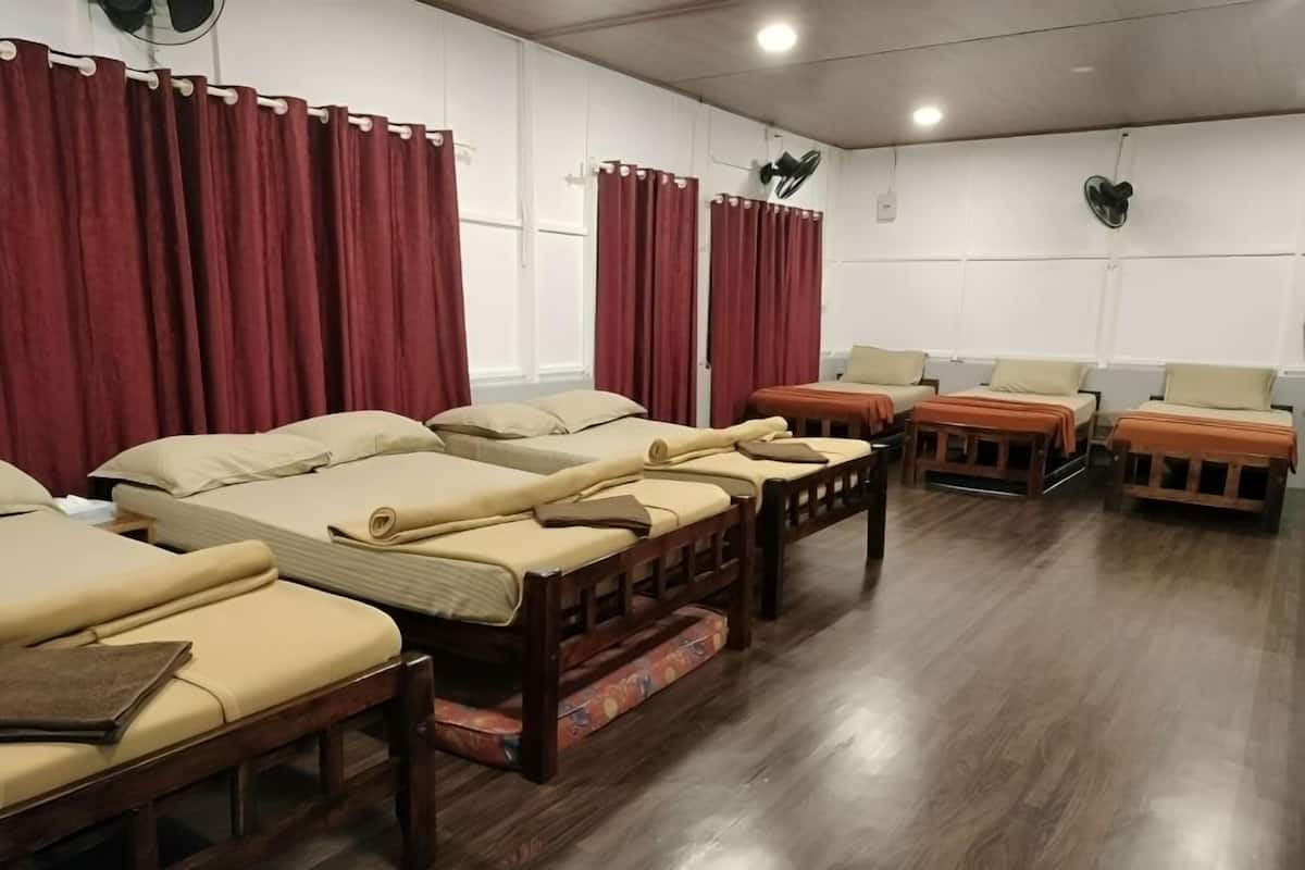 A room with multiple beds, wooden flooring, and red curtains.
