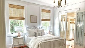 A bedroom with a white bed, bedside tables, a radiator, and a window with a view of greenery. - Pristine Craftsman 1900s Bungalow w Pool & Hot Tub (Savannah)