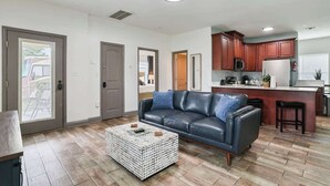 Una sala de estar con un sofá de cuero, una mesa de centro y una zona de cocina con armarios de madera y un microondas.