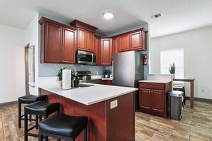 A kitchen with wooden cabinets, a microwave, a refrigerator, a sink, and a bar stool. - Cozy Cottage Near Thunderbolt Marina w Fenced Yard (Thunderbolt)