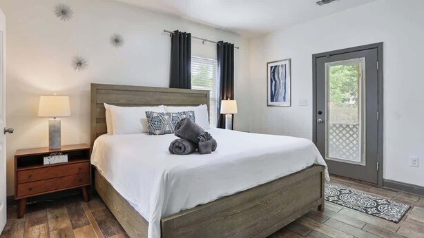 Un dormitorio con cama de madera, dos lámparas de noche, una mesita de noche, una puerta con vistas y una alfombra estampada.