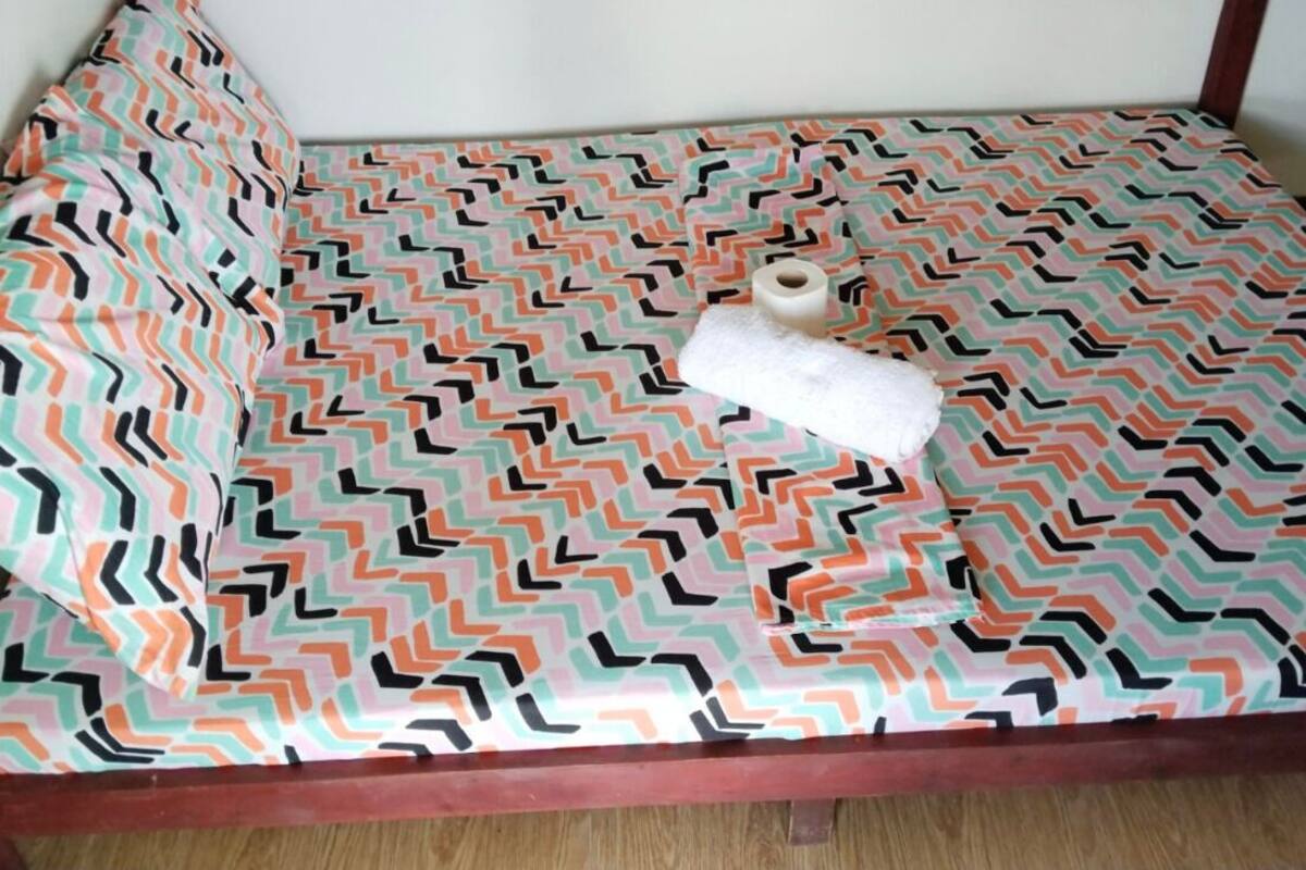 A bed with patterned bedding, a roll of toilet paper, and a pillow.
