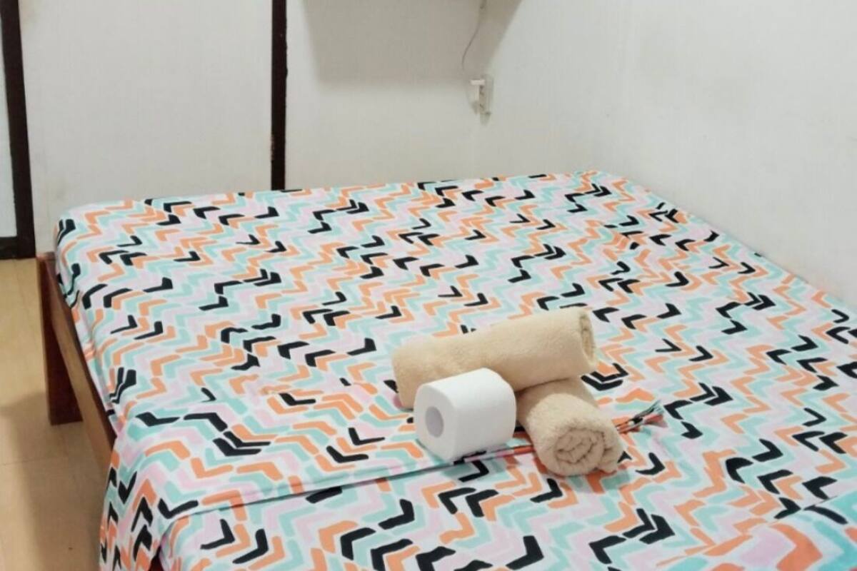 A bed with a patterned bedspread, a rolled-up towel, and a roll of toilet paper on the bed.