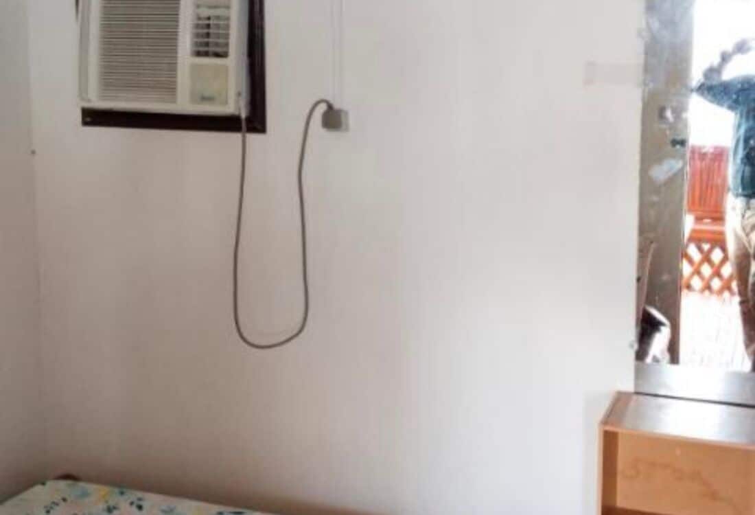 Una habitación con ventana, equipo de aire acondicionado y un armario de madera.