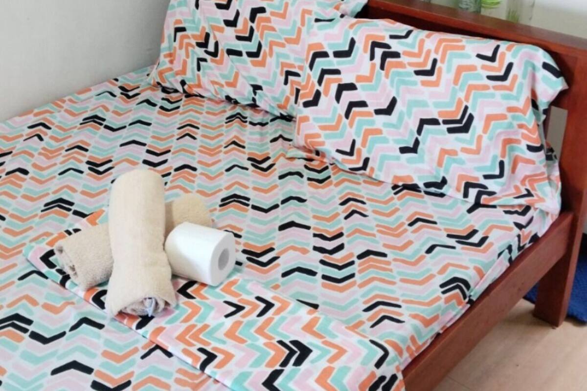 A bed with a patterned bedspread, a rolled-up towel, and a roll of toilet paper.
