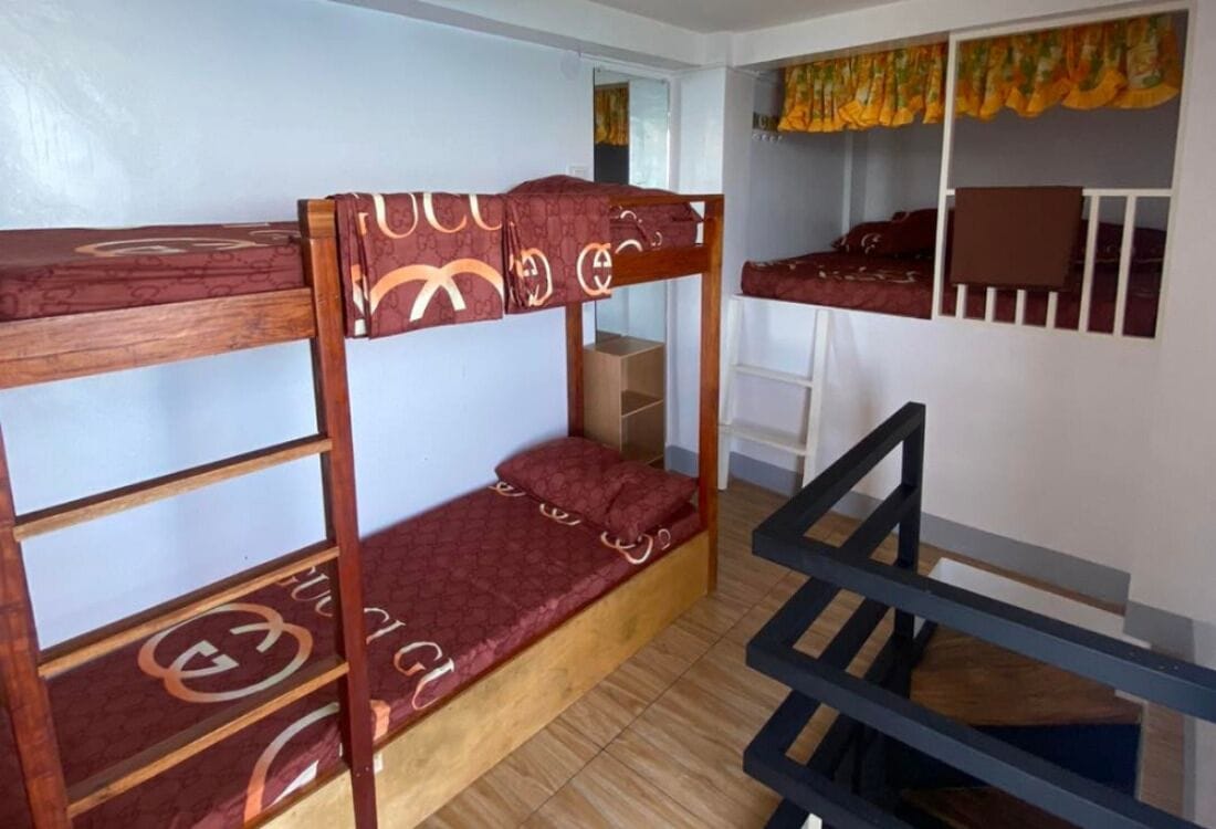 A bunk bed room with a wooden ladder, a wardrobe, and a small table.
