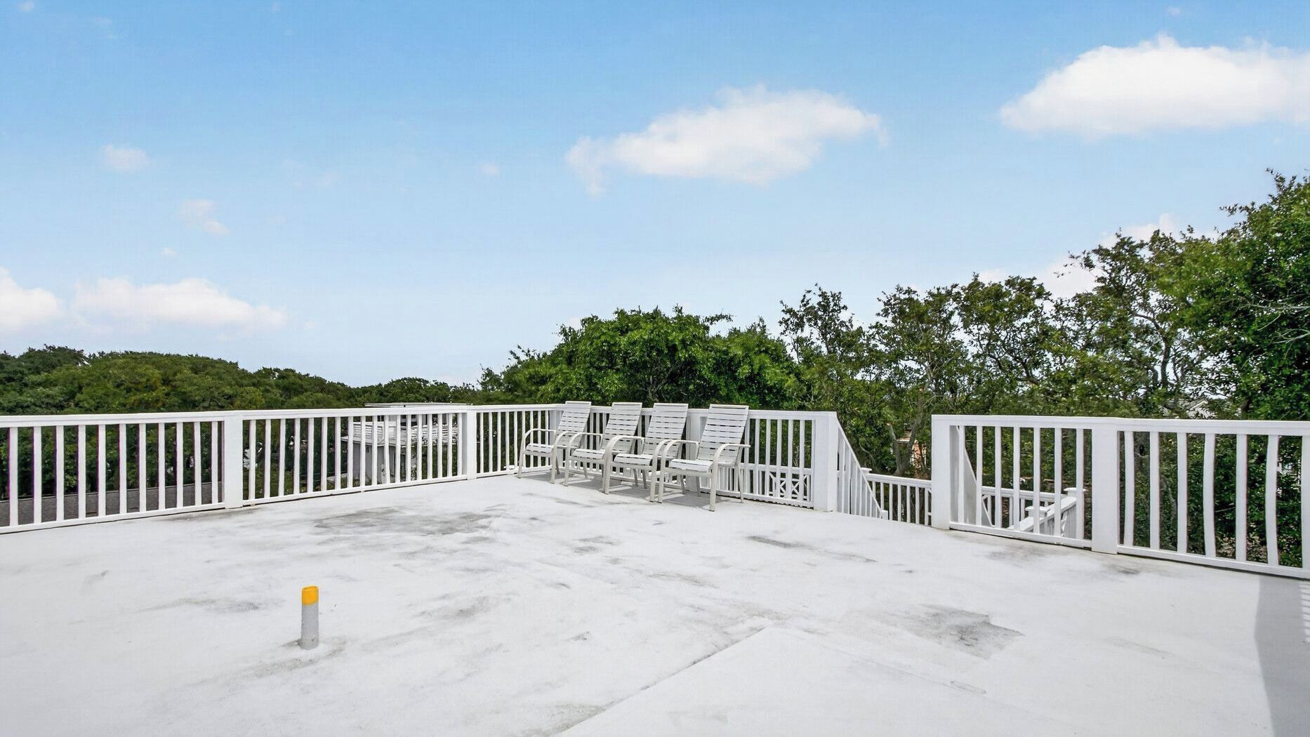 A rooftop deck with white railings and multiple lounge chairs.