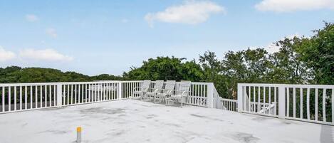 A rooftop deck with white railings and multiple lounge chairs.